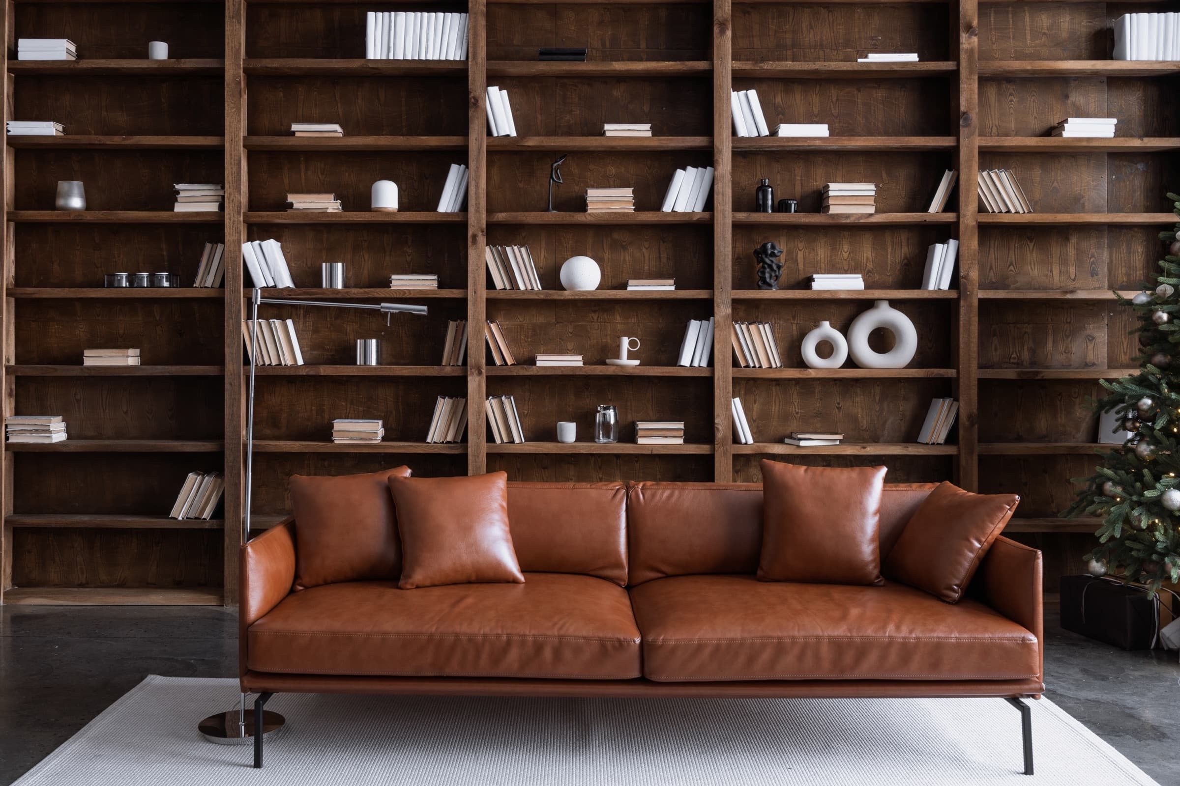 Raumhohe Bücherwand aus dunklem Holz hinter einem Ledersofa